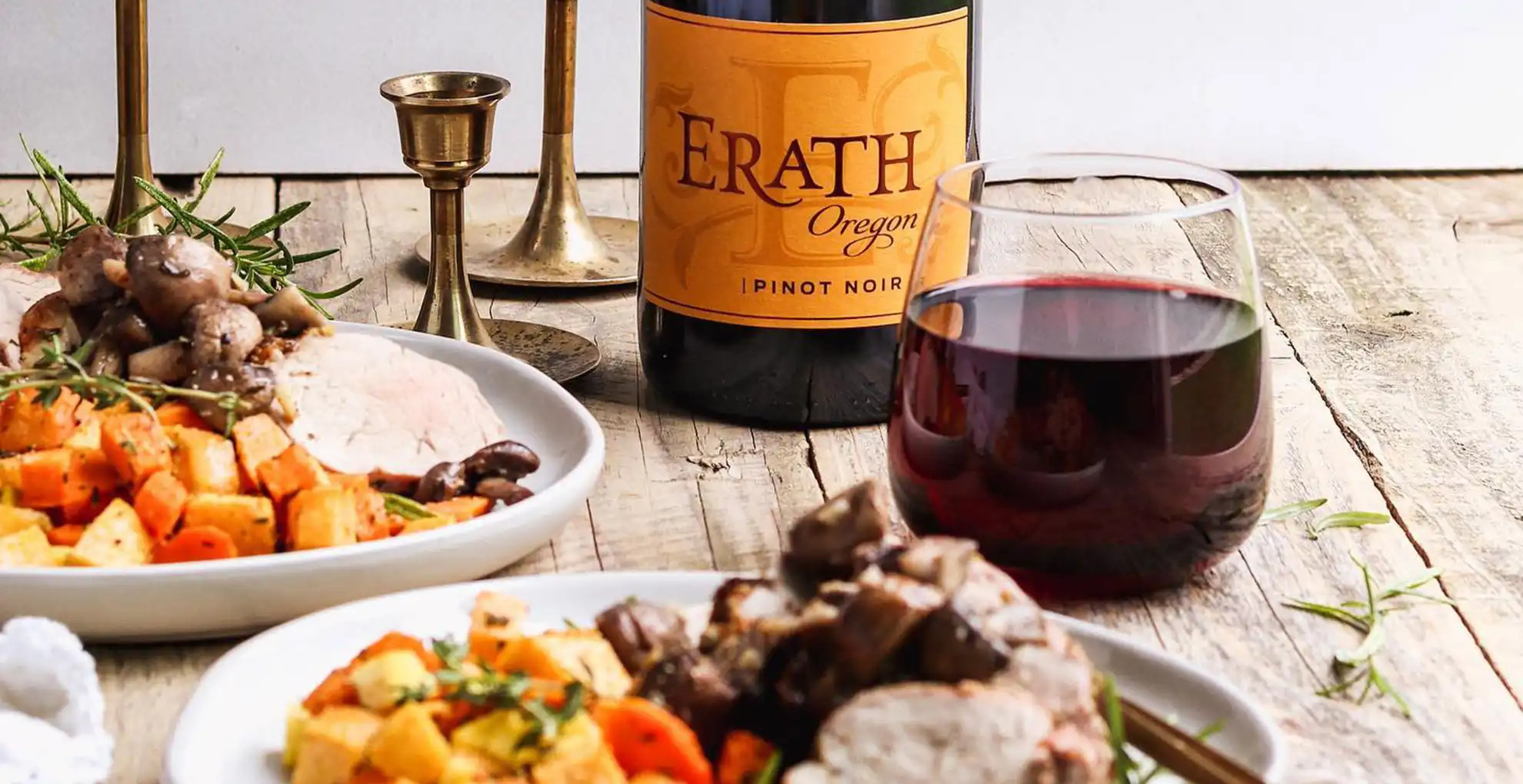 pork and vegetables on two plates, glass of wine next to erath pinot noir bottle