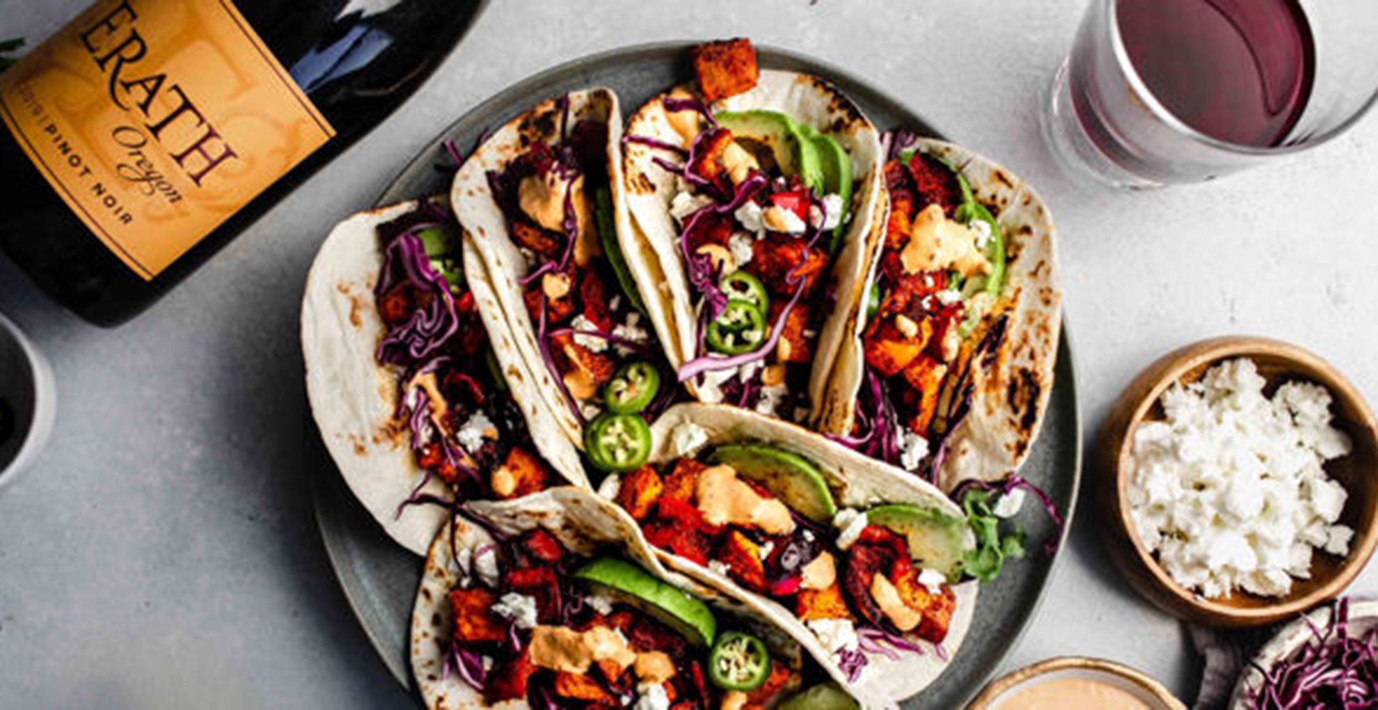 tacos on plate next to bowl of cheese, bottle of pinot noir on top with glass of wine