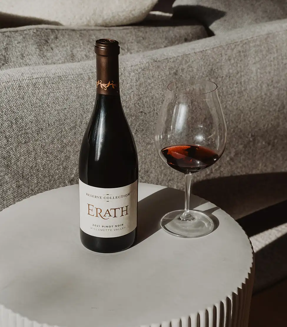 A bottle of Erath Pinot Noir on a table beside a glass of wine.