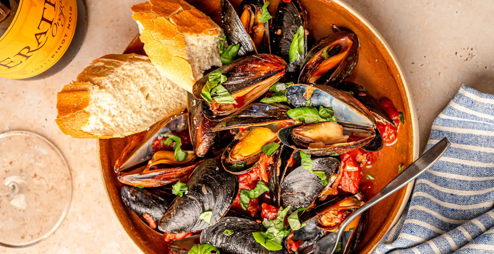 Overhead shot of Mussels Marinara in a Dutch oven, garnished with fresh herbs and served with crusty bread.