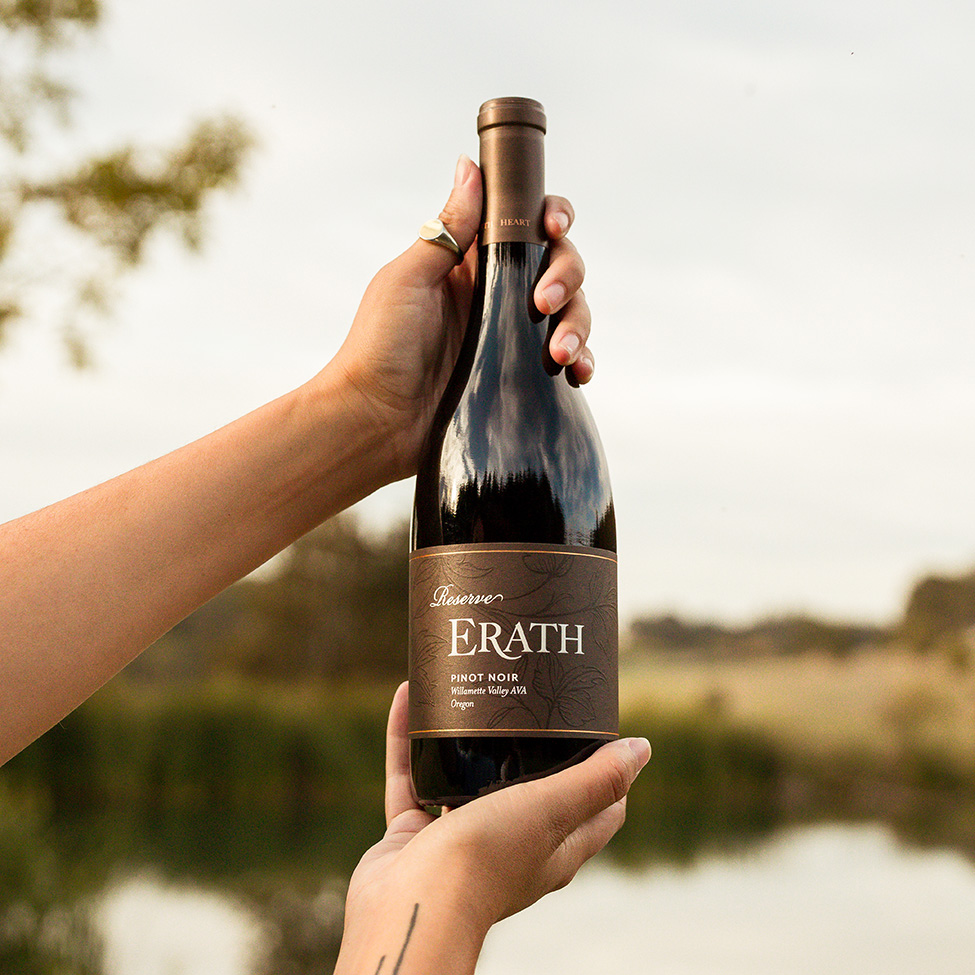 hands holding erath reserve pinot noir outside by lake