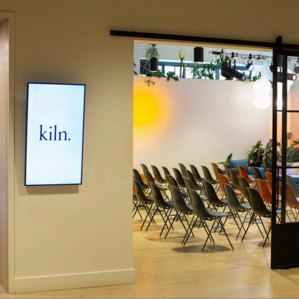 A photo of the theater space at Kiln Portland. A TV with "kiln" is hanging outside a room full of chairs
