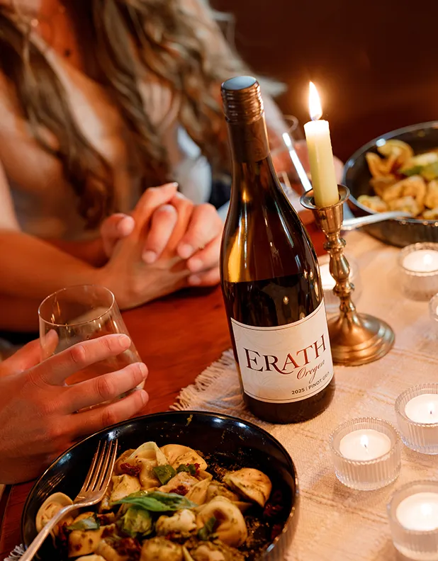 A bottle of Erath Pinot Gris on a table. A man and woman sit at the table holding hands and enjoying their food and wine.